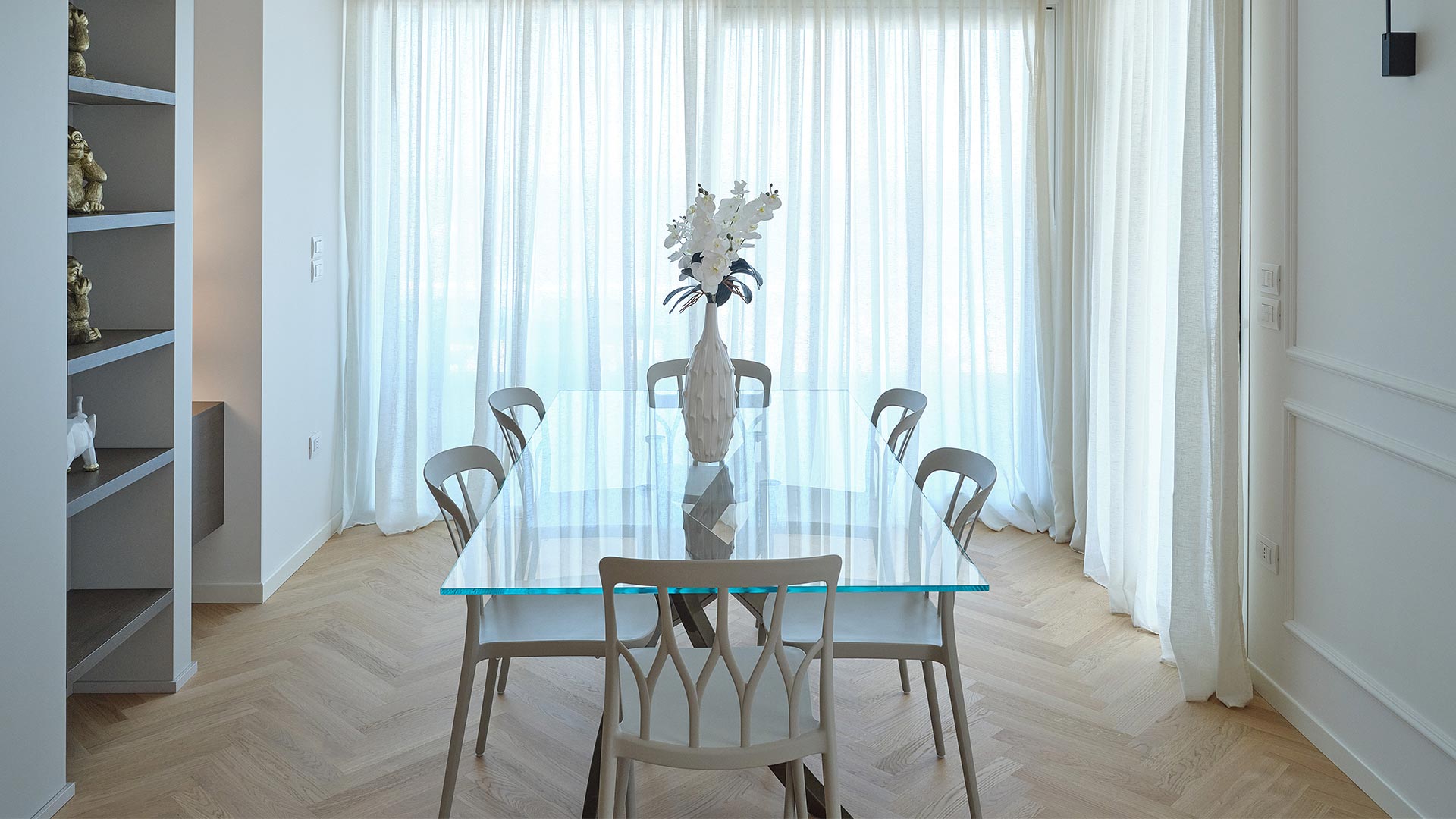 Zona pranzo con tavolo in cristallo, parquet a spina di pesce